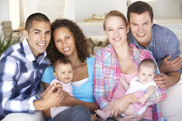 Two Young Family With Babies On Sofa At Home