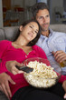 © Monkey Business - Hispanic Couple On Sofa Watching TV And Eating Popcorn