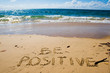 Be positive. Creative motivation concept written in the sand at the beach.