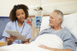 © Monkey Business - Nurse Sitting By Male Patient's Bed Using Digital Tablet