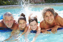 Grandparents With Grandchildren On Airbed In Swimming Pool