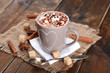 Cup of hot coffee with marshmallow on burlap cloth with lump sugar, sticks of cinnamon and star anise on rustic wooden planks background