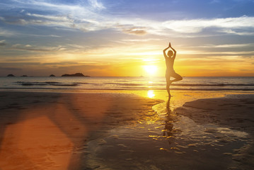 Wall Mural - Woman standing at yoga pose on the beach during amazing sunset.