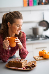 Wall Mural - Woman smiling in kitchen holding mug with fresh fruit loaf