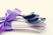 Three metal spoons on a napkin are tied with a lilac tape in peas on a light background