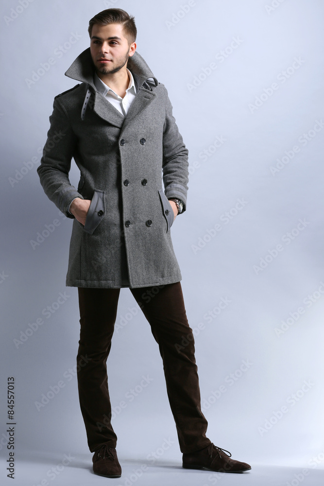 Young man in coat on gray background