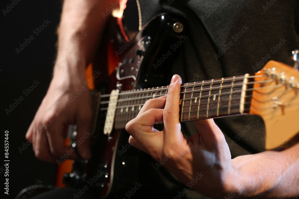 Young man playing on electric guitar on dark background