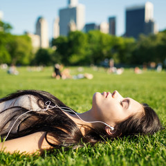 young woman relaxing in central park laying on the grass and listening to music.