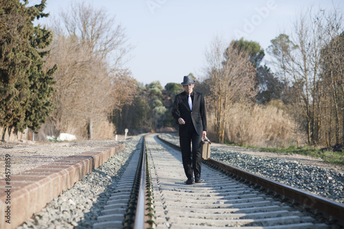 Fotografie, Obraz Hombre con traje y maleta antiguos camina por raíles de tren
