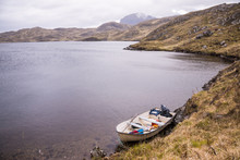 White Fishing Boat Near The Shore Of A Wild Loch 