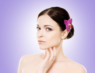 Beautiful face of a young and healthy girl with an orchid flower in her hair over blue background