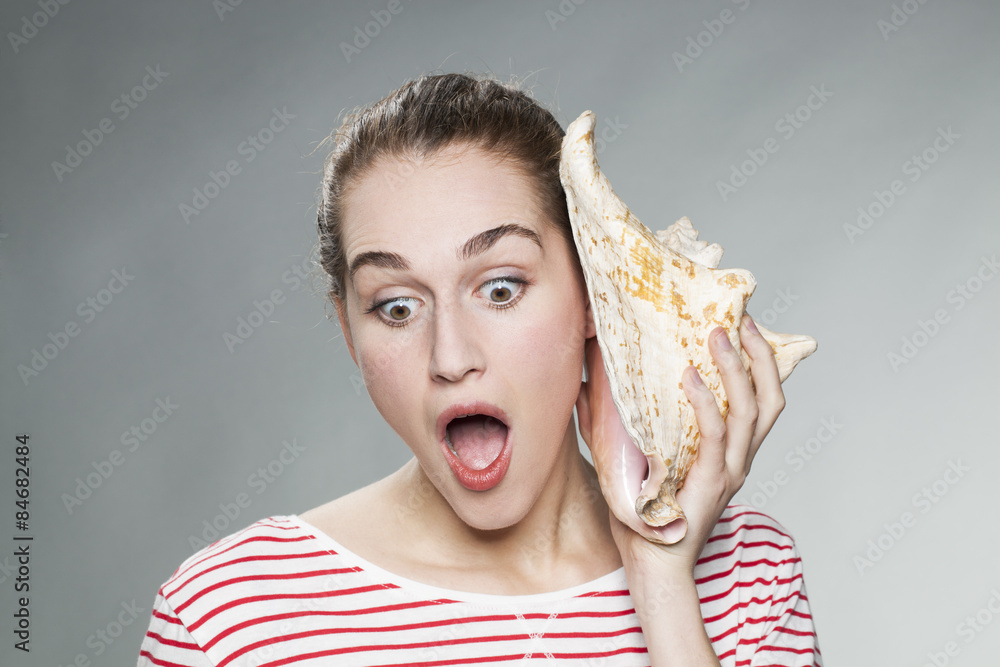 young girl stunned about the sound coming from a big shell to her ear ...
