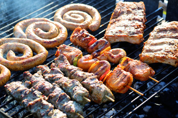 Assorted mixed grill on wooden skewers from chicken meat, lamb and pork, marinated spareribs, sausages and various vegetables roasting on barbecue grid cooked for summer family dinner