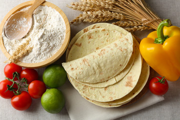 Poster - Stack of homemade whole wheat flour tortilla and vegetables on light background