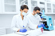 © Syda Productions - scientists with clipboard and microscope in lab