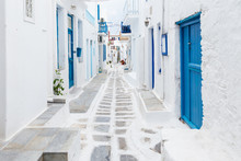 Mykonos, Greece - Traditional Whitewashed Street Of Mykonos Town With Blue Windows And Doors On A Sunny Summer Morning. Empty Alleyway At Sunrise