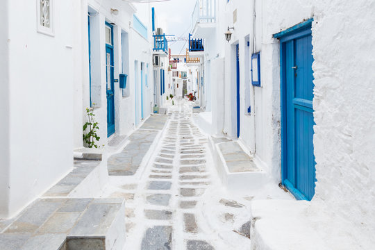 mykonos, greece - traditional whitewashed street of mykonos town with blue windows and doors on a su