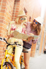 Two girl friends using map while riding tandem bicycle