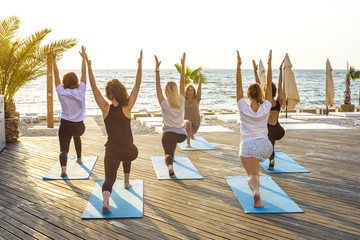 group of young females practicing yoga on the seaside during the sunrisе