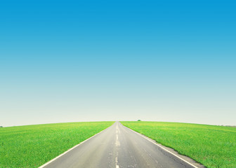 Asphalt road through the green field and blue sky