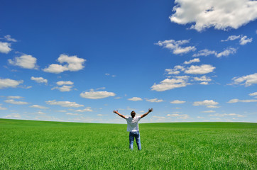 man with arms raised on a green field under beautiful sky