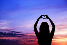 Female Silhouette With Raised Hands In A Heart Shape Against The Sky