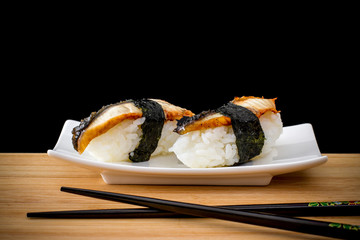 Two nigiri eel sushi with chopstick on bamboo board