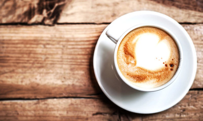 Poster - Cup of coffee with heart pattern in a white cup on wooden backgr