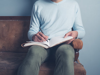 Young man sitting on old sofa writing