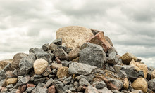 Big Pile Of Rocks And Boulders Piled In A Heap Under A Grey Dark Cloudy Sky In Summer Time