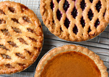 Three Pies On Cooling Racks. High Angle Closeup Shot Of Fresh Baked Apple, Cherry And Pumpkin Pies On Wire Racks On A Rustic Wood Kitchen Table. Horizontal Format.