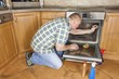 © martinfredy - Man kneels on the floor in the kitchen and cleans the oven. Cleaning work in the home. Man helping his wife with maid service.