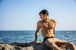 © theartofphoto - Young shirtless athletic man crouching in water by ocean shore