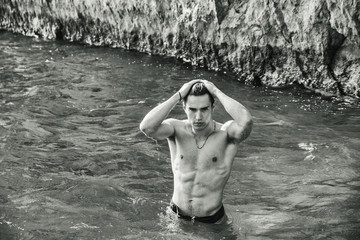 Young shirtless athletic man standing in water by ocean shore