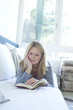 © Westend61 - Woman lying on couch reading a book