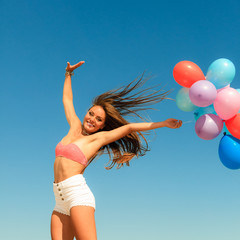 Girl jumping with colorful balloons on sky background