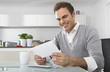 © Westend61 - Smiling man sitting in kitchen watching envelope