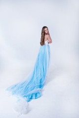 beautiful girl in a blue long dress with plume on a white backgr