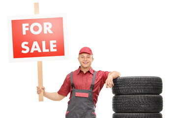 Wall Mural - Cheerful male mechanic standing by a pile of tires and holding a