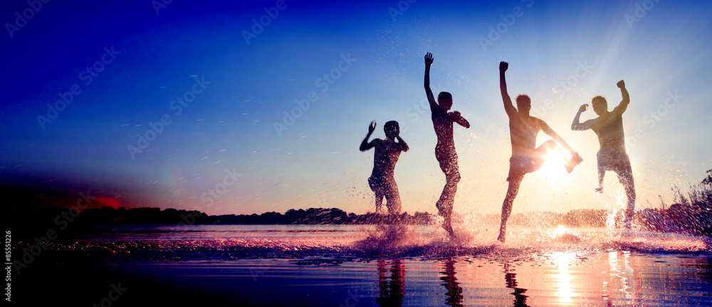 Glückliche junge Menschen laufen und springen am See beim Sonnenuntergang - obrazy, fototapety, plakaty 