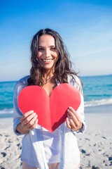 Smiling woman holding heart card at the beach