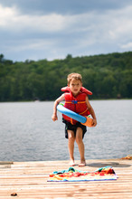 Little Boy Standing On A Dock By A Lake Wearing A Life Jacket And A Float Ring