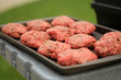 A tray of raw beef hamburger patties waits by the grill in the middle of summer