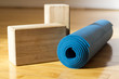 Yoga Mat and Blocks - Yoga Accessories in Studio. A blue yoga mat with two wooden yoga blocks sit on a wooden yoga studio floor before class.