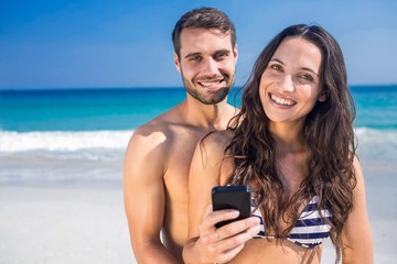 Wall Mural - Smiling couple using smartphone at the beach