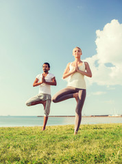 Canvas Print - smiling couple making yoga exercises outdoors