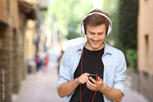 Fotografia Guy walking and using a smart phone with headphones