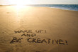 Wake up and be creative! Creative motivation concept written in the sand at the beach.