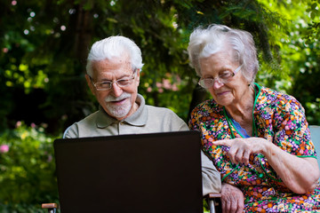 Elderly couple having fun with the laptop outdoors