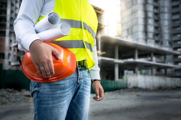 engineer with hardhat and blueprints posing on building site